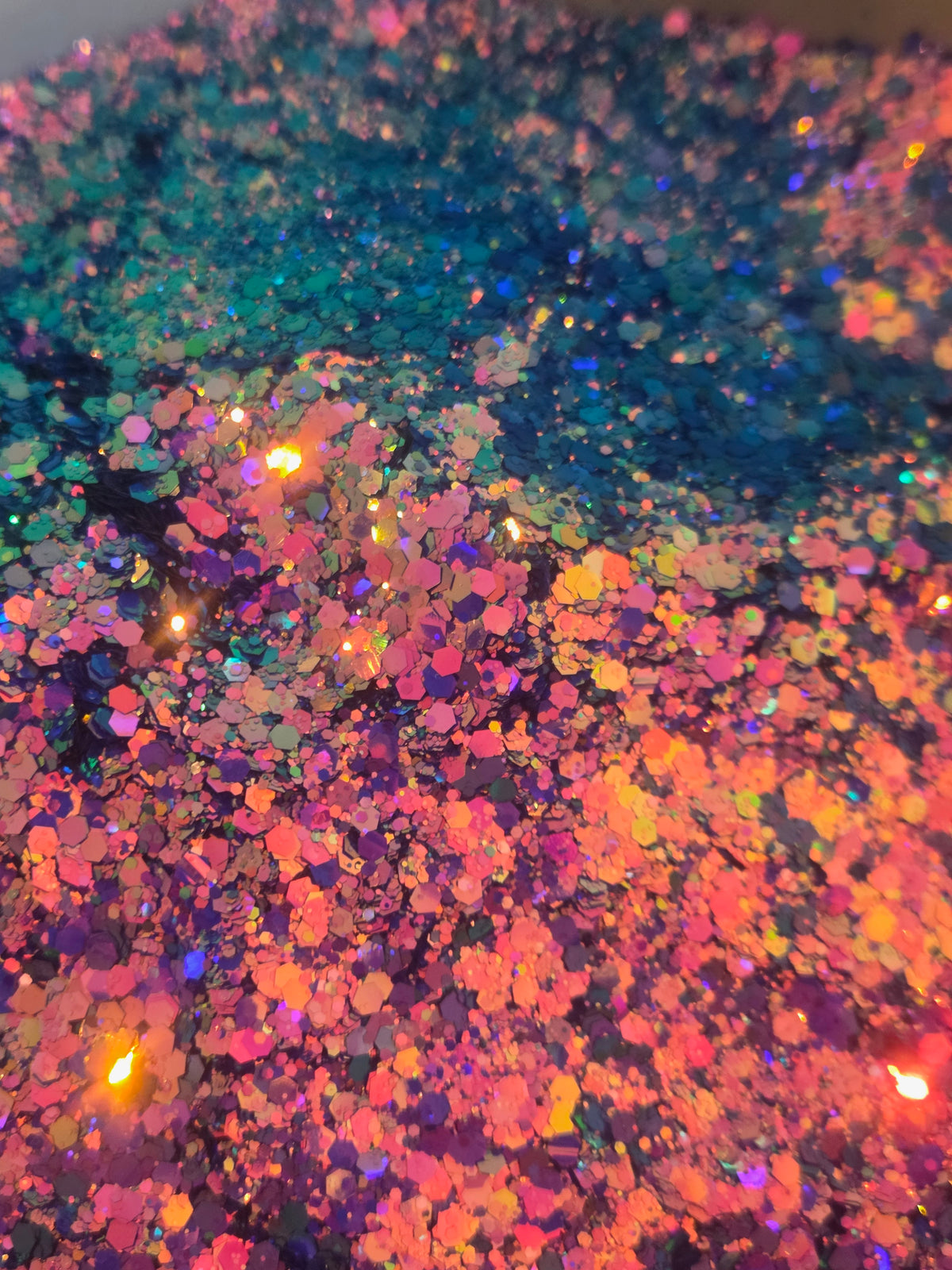 Close-up of iridescent glitter flakes with a color-shifting finish, showing a mix of pink, orange, purple, blue, and green tones.