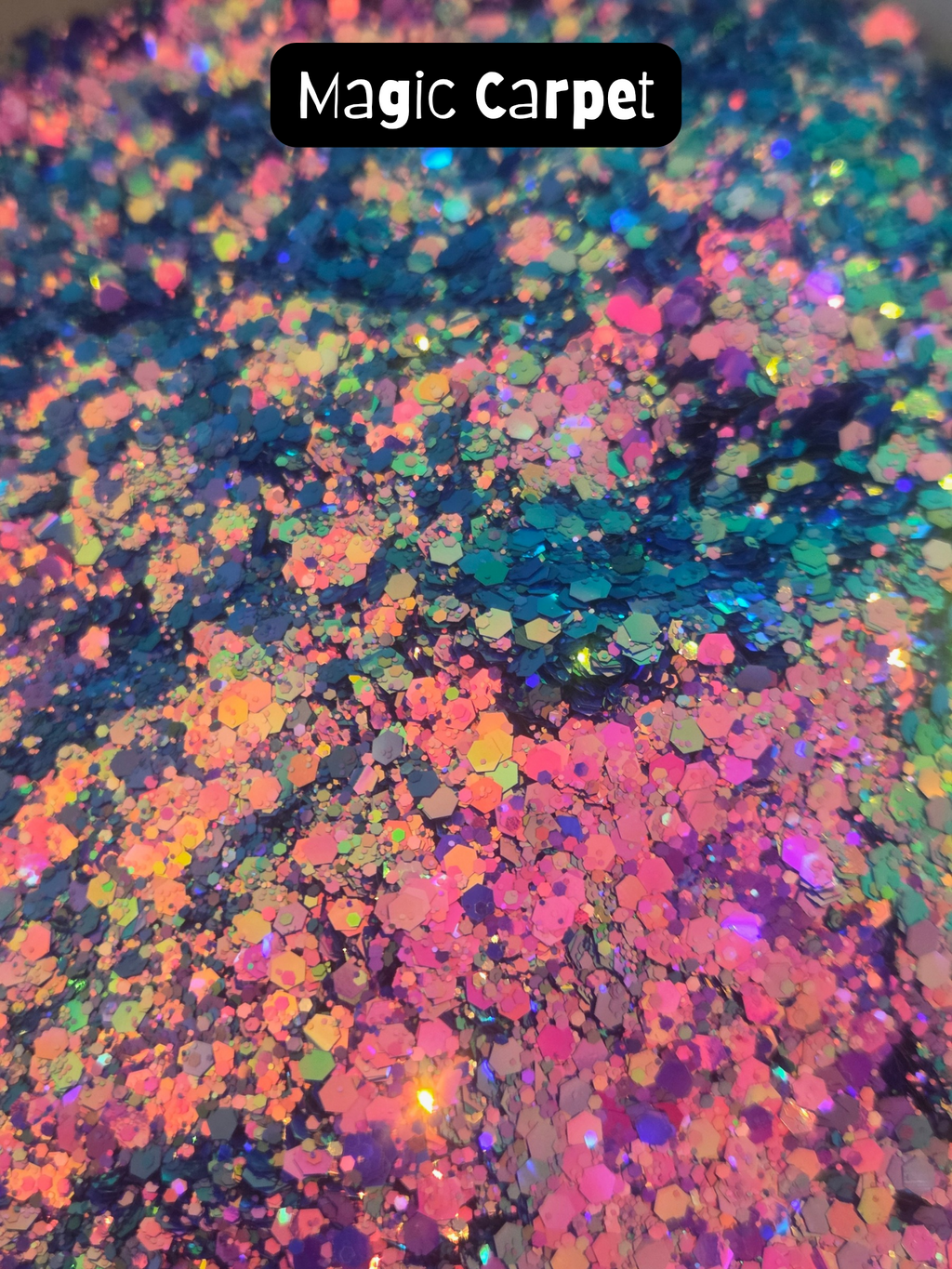 Close-up of a multicolor iridescent hexagonal glitter blend labeled 'Magic Carpet' in a black text box at the top. The glitter reflects pink, blue, green, orange, and purple tones over a dark base.