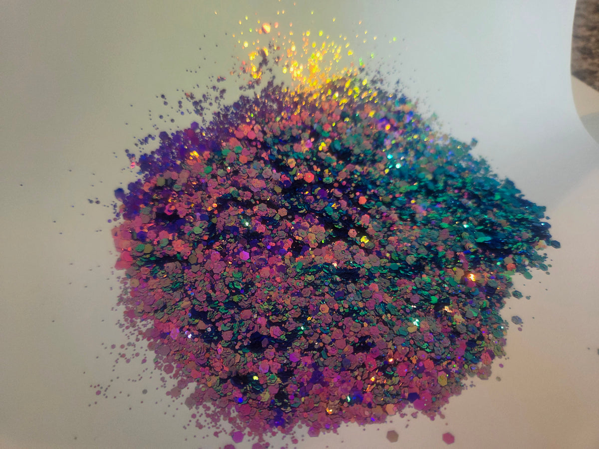 A pile of iridescent glitter with a rainbow of colors including pink, purple, blue, green, and gold, scattered on a plain white surface.