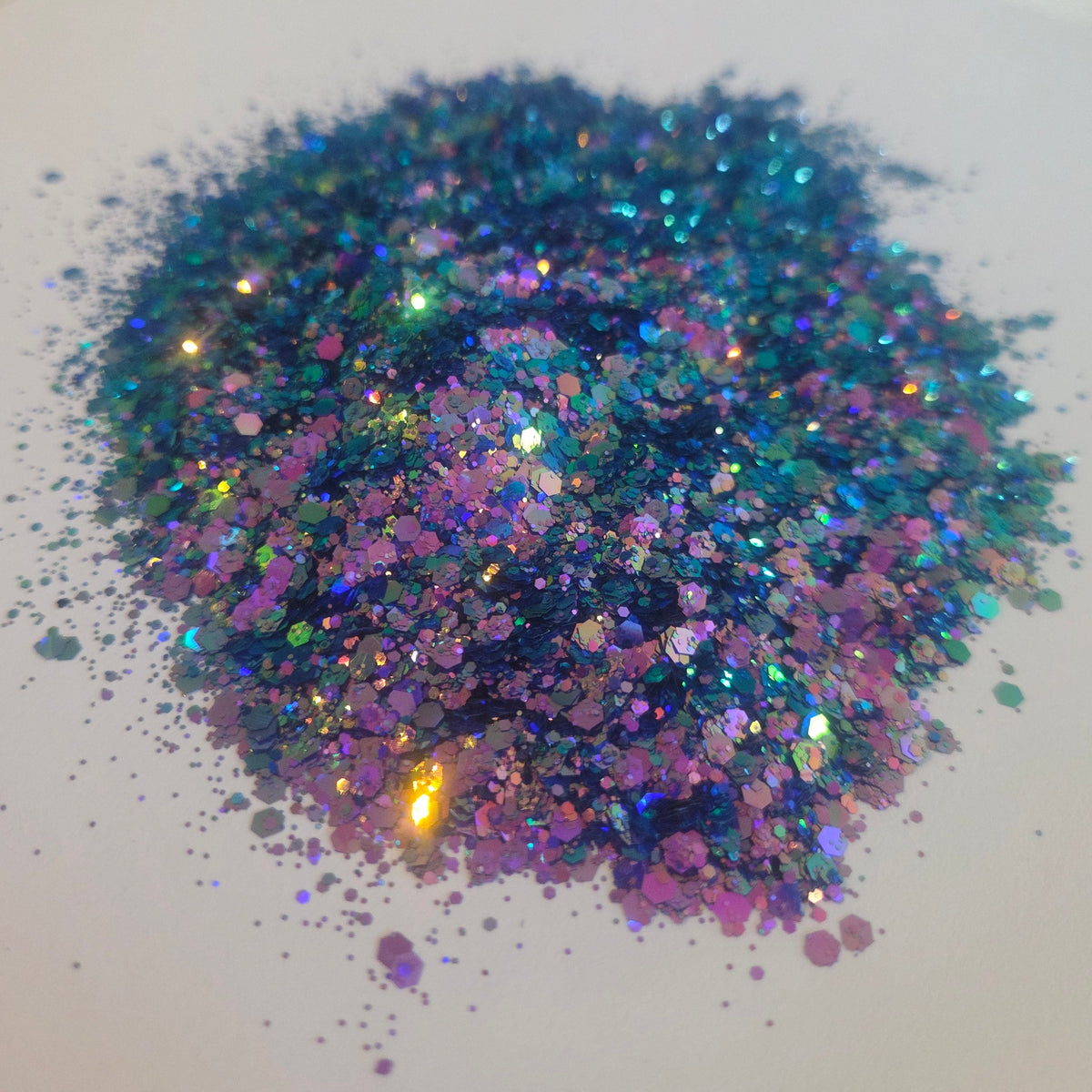 A pile of iridescent holographic glitter flakes in shades of blue, purple, pink, and green, scattered on a plain white surface.